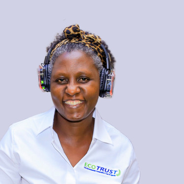 A woman in a white shirt sits smiling in front of an off-white wall