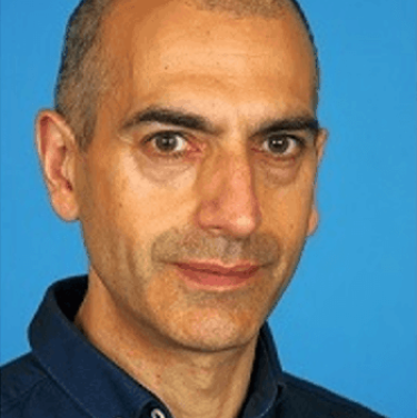 A man in a dark blue shirt stands in front of a light blue background