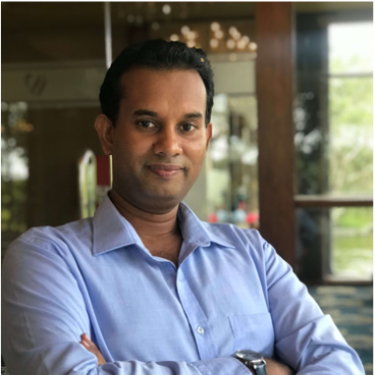 A man in a light blue shirt stands in front of a window