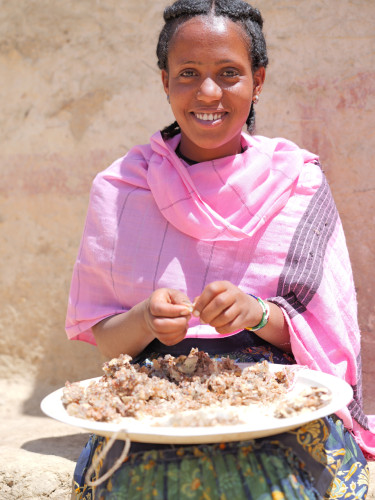 A woman in a pink scarf smiles at the camera as she sorts frankincense in a bowl