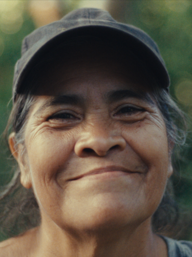 A woman in a baseball cap smiles at the camera with out of focus trees behind her