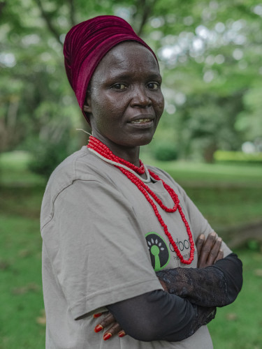 A woman in a red headscarf stands side-on looking at the camera