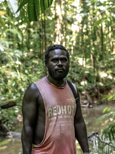 A man in a pink sleeveless t-shirt stands on a path in a forest