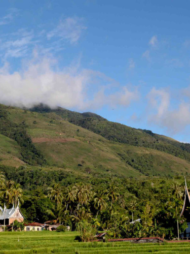 A group of house with pointed roofs in front of wooded hills and a blue sky above