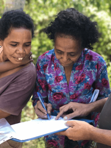 Two women sign a book with plants in the background