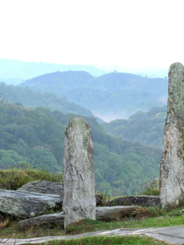 A group of standing stones with misty wooded hills in the background