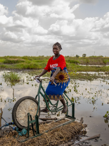 A woman is sitting on a bicycle which is part of an irrigation apparatus in front of a body of water