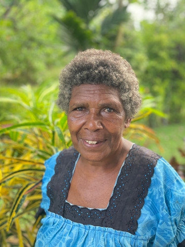 A woman in a blue dress stands with plants in the background