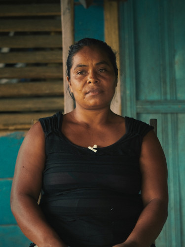 A woman in a black sleeveless top sits outside a wooden building painted blue