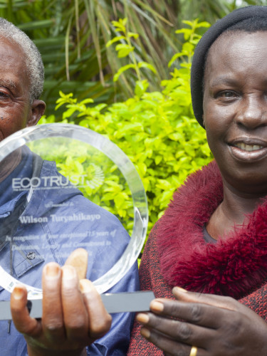 Two people holding a glass award in front of a forest