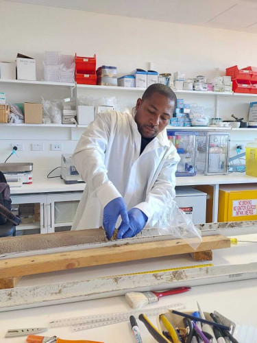 A man in a white coat stands in a lab analysing a soil sample