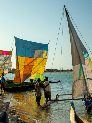 Small boats with colourful patchwork sails on the edge of the beach with some people