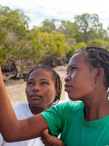 Two young women hold up a device on a beach