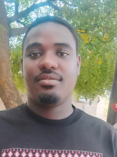 A man in a black t-shirt stands in front of a traditional shield