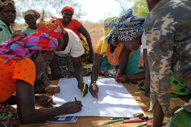 A group of people sit on the floor and write on a big sheet of paper