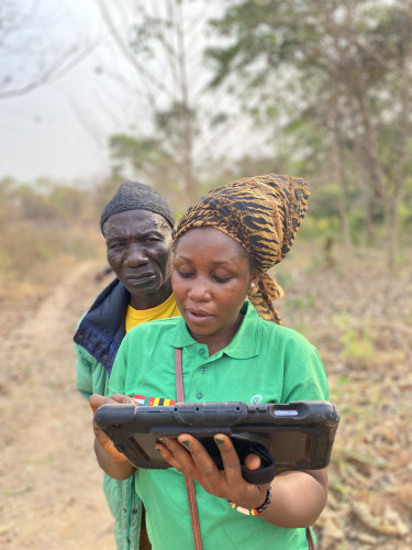 A woman in a headscarf is typing something on an electronic tablet while a man looks over her shoulder
