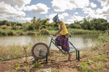 A woman pedals a specially adapted irrigation bike on the banks of a river