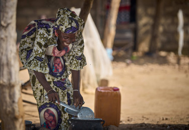 A woman cleans a watering can outside a building