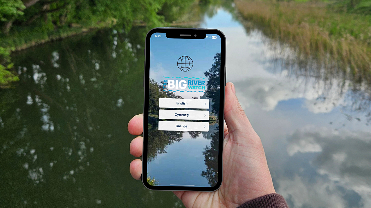 Hand holding mobile phone displaying Big River Watch app with river in background