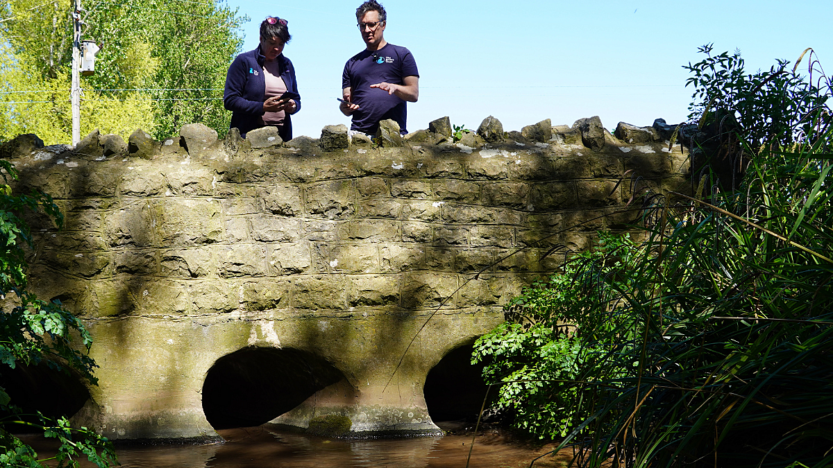 Man and woman stood on stone bridge overlooking river