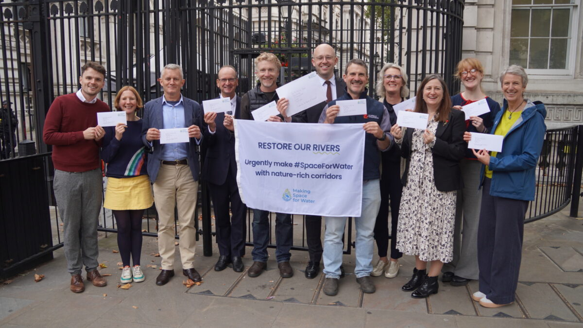 A group of people stood in front of black gates holding a white flag and envelopes