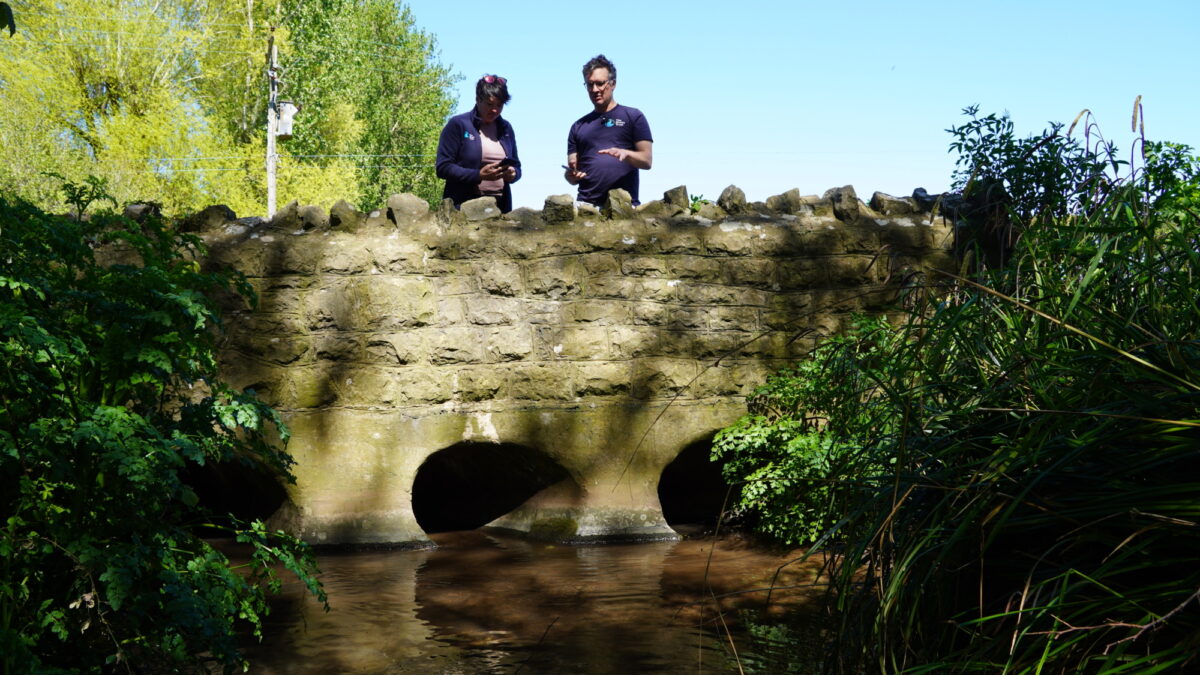 Man and woman stood on a stone bridge over a river