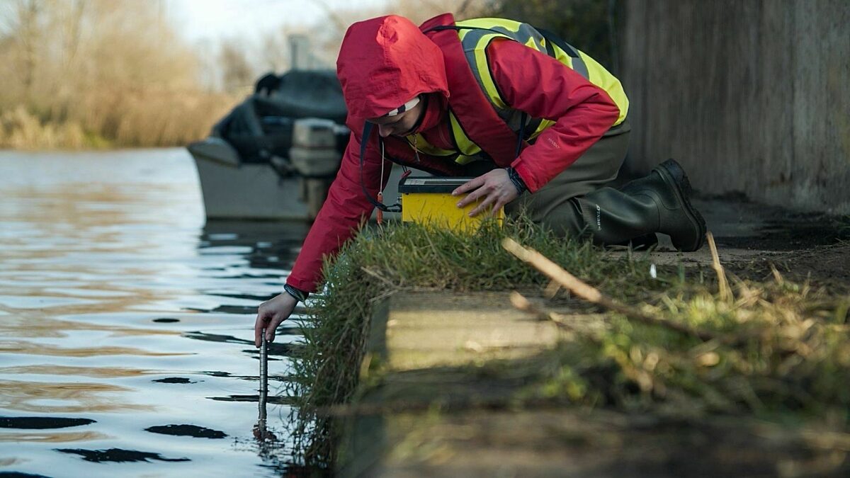 Person in waterproof jacket and high vis vest using a test tube to monitor a river