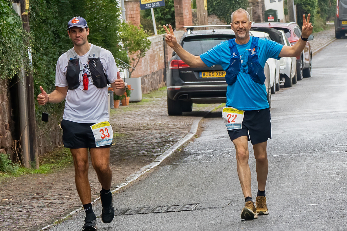 Two male runners, left one in white top, right in blue top, running towards the camera