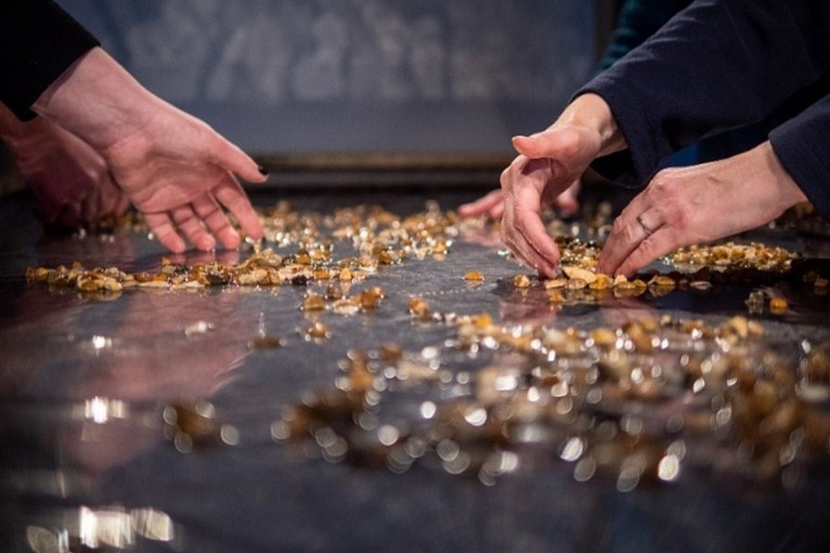 Two pairs of hands gathering small orange petals on a table