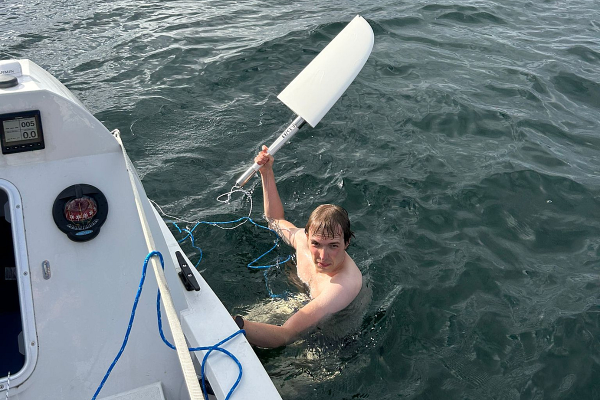Topless man in the sea next to a rowing boat holding a rudder