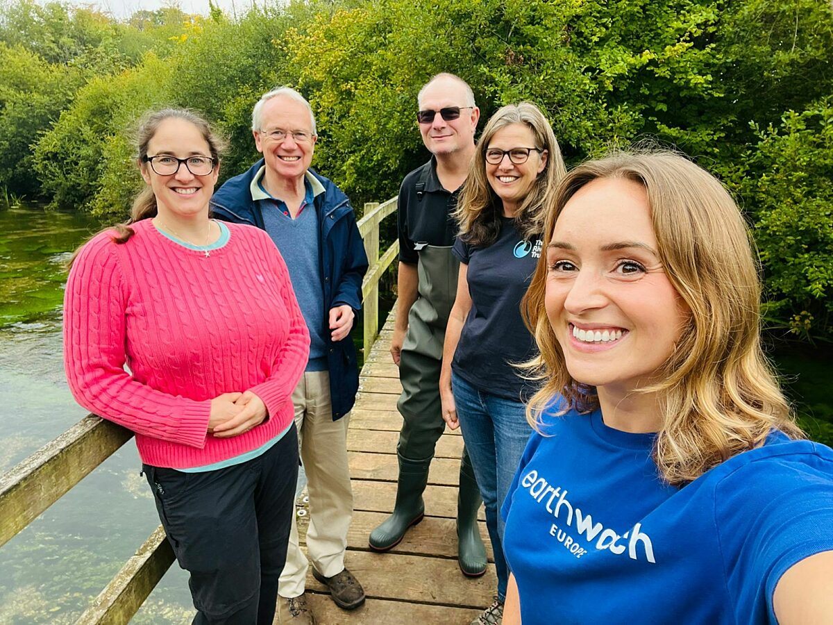 five smiling people stand on a bridge facing the camera