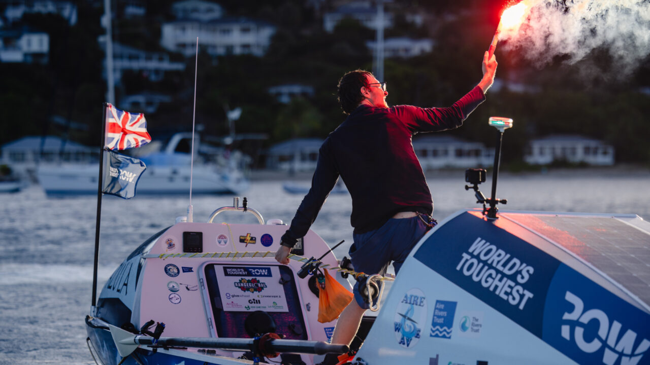 Man stood up holding flare on boat pulling into harbour