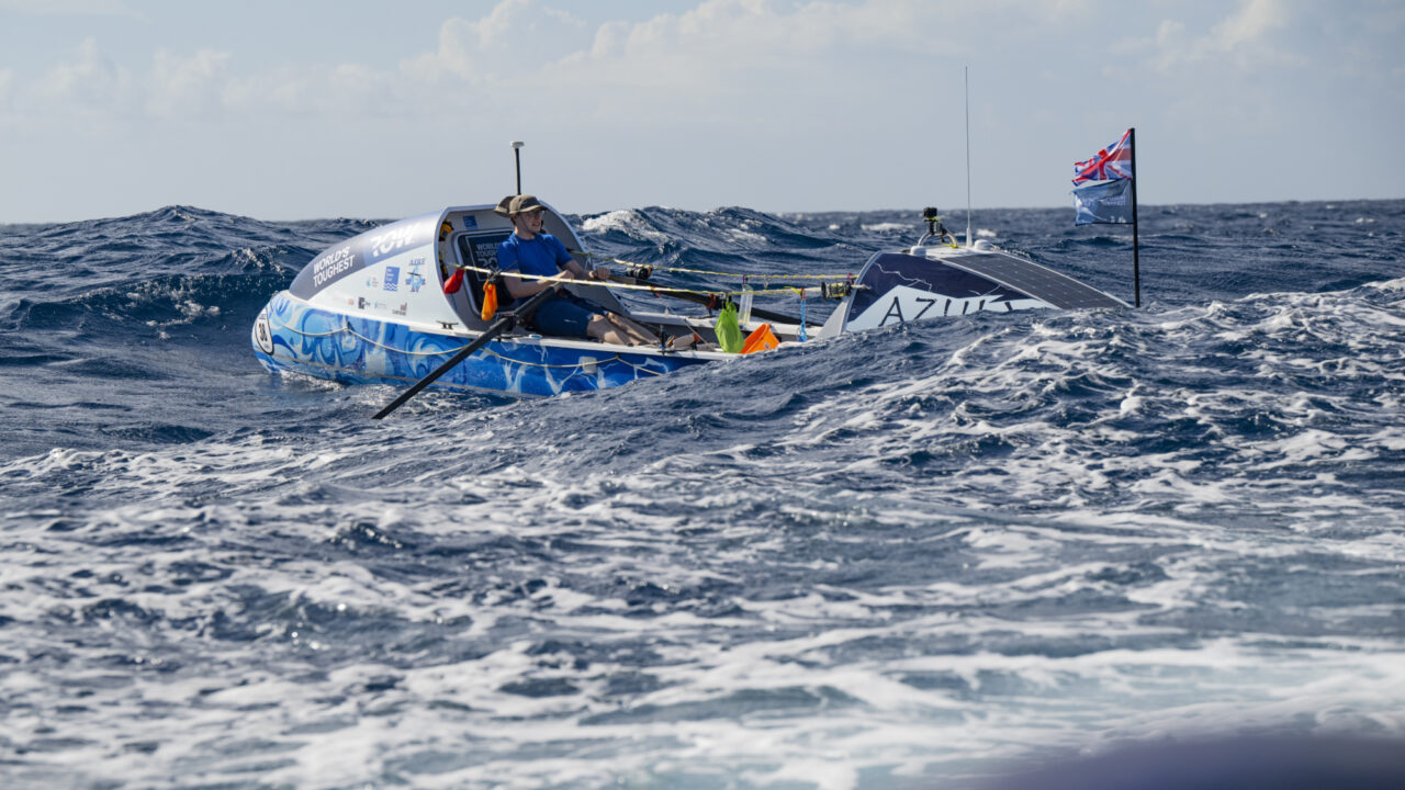 Man in blue shirt rowing across open ocean in choppy conditions