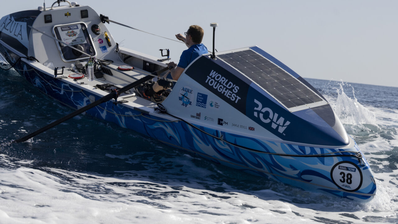Man rowing across open ocean with boat at high angle from waves