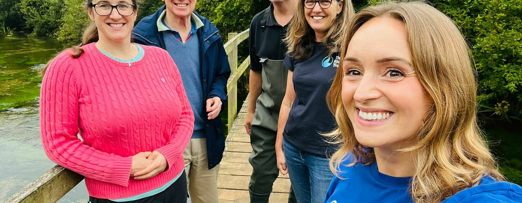 five smiling people stand on a bridge facing the camera