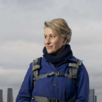 A smiling woman stands on the foreshore of the thames