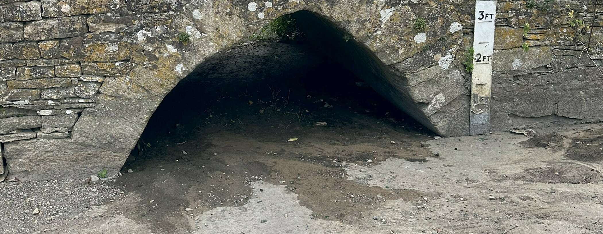 a bridge over a dried up river ford is shown with a height marker to one side