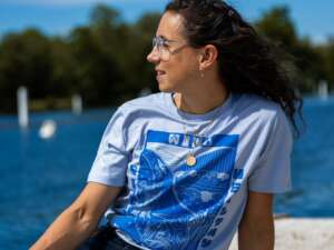 Imogen Grant sits on a dock by the river wearing a light blue tee with stylish dark blue river design