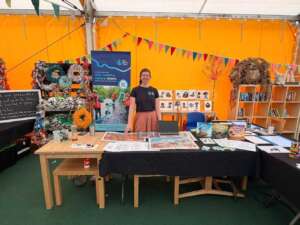 A smiling woman in a Rivers Trust teeshirt stands at a craft stall