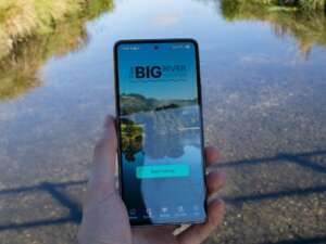 Hand holding a phone with an app reading Big River Watch with a river in the background