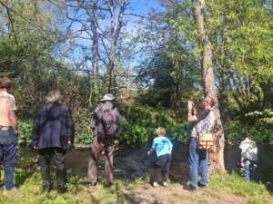 Group of people stood on a river bank looking at the water with trees around them