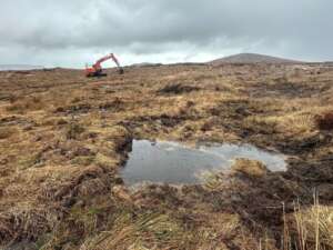 Pool of water on a peatland in the foreground and a digger in the background
