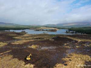 Ariel view of a peatland with a yellow digger in the foreground and a river in the background