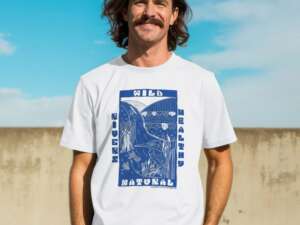 A smiling man stands in the sunshine, wearing a white tee with a bold navy print