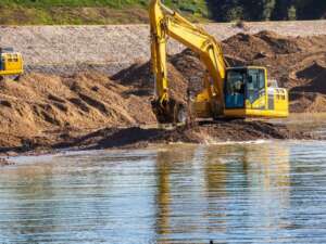 Yellow digger on the bank of a river pulling up gravel