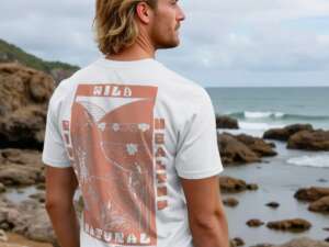 A smiling man wears a white teeshirt with a salmon peach design