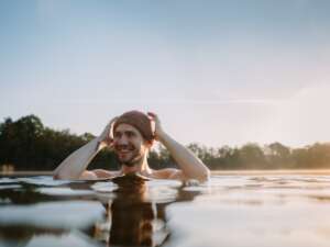 Young man swims in a river with a hat on