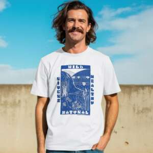 A smiling man stands in the sunshine, wearing a white tee with a bold navy print