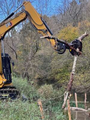Yellow digger holding a branch next to a river