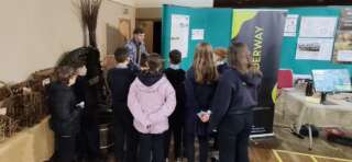 Group of people stood next to each other looking at an event stands listening to a speaker